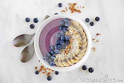 Blueberry smoothie bowl with coconut, bananas, chia seeds and granola, flat lay on marble Stock Photo
