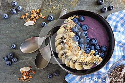 Blueberry smoothie bowl with coconut, bananas, chia seeds and granola, above view on a dark background Stock Photo