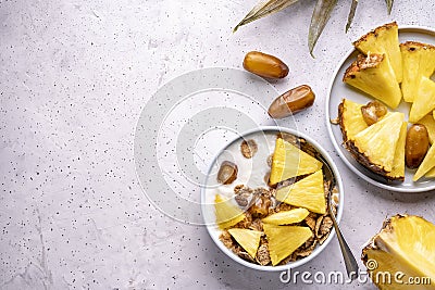 Healthy breakfast bowl: dates with fresh pineapple homemade granola corn flakes on light grey background. Flat lay selective Stock Photo