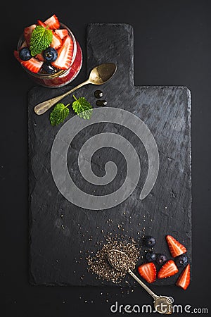 Healthy breakfast food frame. Chia pudding with fresh berries and mint on black slate stone board over dark background Stock Photo