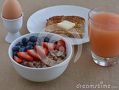 Healthy Breakfast Scene with grapefruite juice, boiled egg, sprouted grain toast, and steel cut oatmeal with fruit. Stock Photo