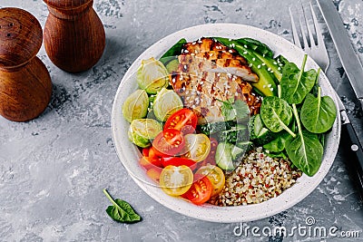 Healthy buddha bowl lunch with grilled chicken, quinoa, spinach, avocado, brussels sprouts, tomatoes, cucumbers on dark grey back Stock Photo