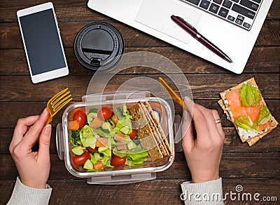 Healthy business lunch at workplace. Salad, salmon, avocado and bread crisps lunch box on working desk with laptop, smartphone, Stock Photo