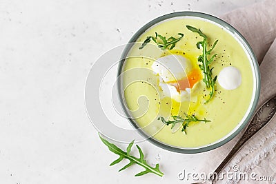 Healthy cauliflower soup with poached egg, olive oil and arugula in a ceramic bowl. Light grey concrete background. Stock Photo