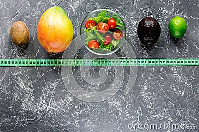 Healthy diet. Salad with fresh products and fruits mango, mangosteen, kiwi and measuring tape on stone table top view Stock Photo