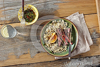 Healthy dinner table concept Beef steak grilled pearl barley couscous wooden table sauce water with lemon top view Stock Photo