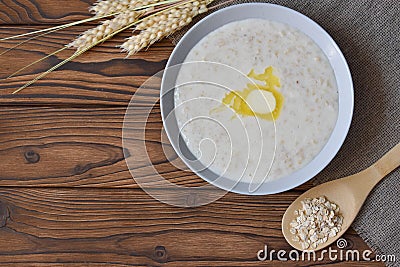 Breakfast: oatmeal with butter, top view. Flakes in a wooden spoon. Stock Photo