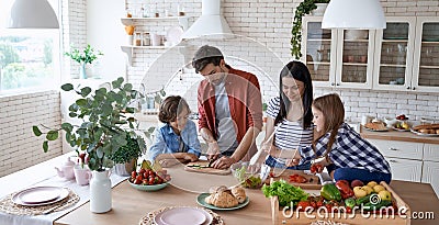 Healthy eating. Young beautiful family cooking together in the modern kitchen at home. Mother and father teaching two Stock Photo