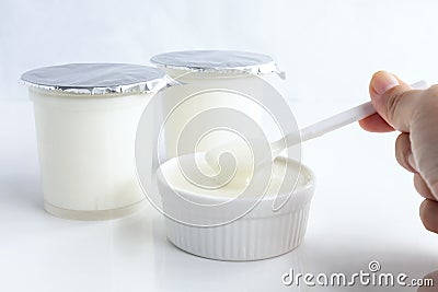 Healthy flavored yogurt on spoon in the woman hand holding and in ceramic bowl with package plastic cup on white background. with Stock Photo