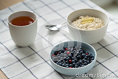 Healthy food breakfast with oatmeal porridge in bowl with summer berries, slice of butter, mug tea. Stock Photo