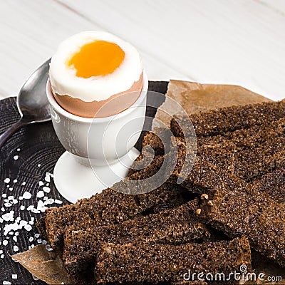 Healthy food. A boiled egg in a white ceramic stand stands on a wooden table next to rye croutons and white sauce Stock Photo