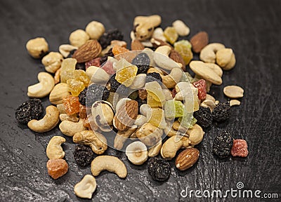 Healthy food; hazelnuts, almonds, cashew, raisin and dried fruits on a stone black background. Stock Photo