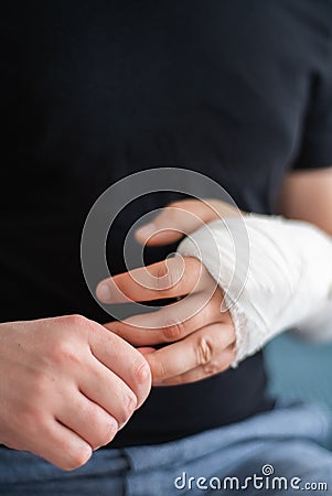 A healthy hand of a young man does a massage of a broken arm in gypsum. Recovery of injured arm after close-up fracture Stock Photo