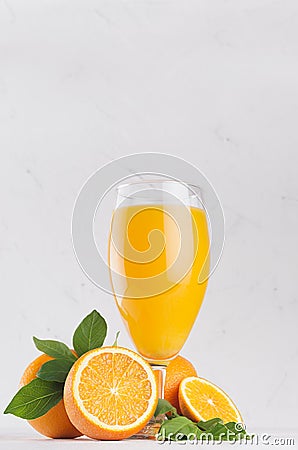 Healthy homemade lemonade - orange juice in wineglass with oranges and green leaves on white wood background, vertical. Stock Photo