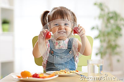 Healthy kids nutrition concept. Cheerful toddler girl sitting at table with plate of salad, vegetables, pasta in room Stock Photo