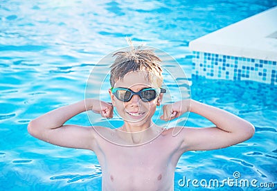 Healthy lifestyle. Active nine years old child boy in sport goggles in swimming pool. Child shows muscles, health force. Stock Photo