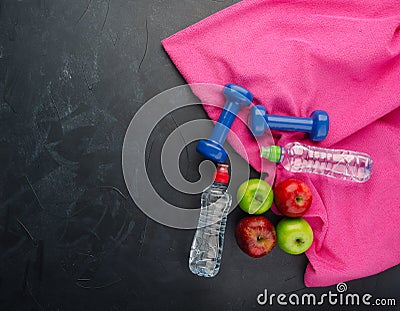 colored Apples dumbbells sport water bottles and purple towel on black concrete background Stock Photo