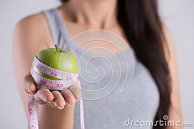 Healthy lifestyle, food and sport concept. Close up young woman hand holding measuring tape around fresh green apple Stock Photo