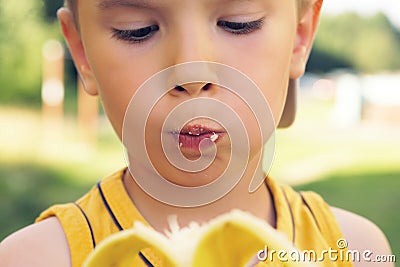 Healthy little boy eating bananaon nature background. Happy kid enjoy eating fresh fruit. Stock Photo