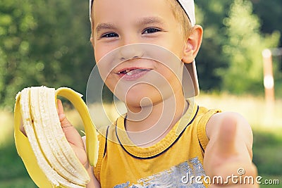 Healthy little boy eating banana. Happy kid enjoy eating fresh fruit and showing thumbs up. Stock Photo