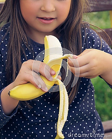 Healthy little girl eating banana. Happy kid enjoy eating fresh fruit. Stock Photo