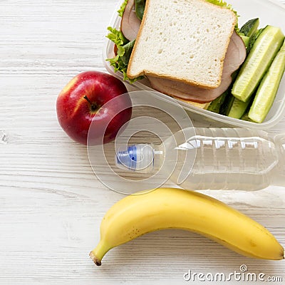 Healthy lunch box with sandwich, fruits and bottle of water on white wooden surface, top view. From above, flat, overhead Stock Photo
