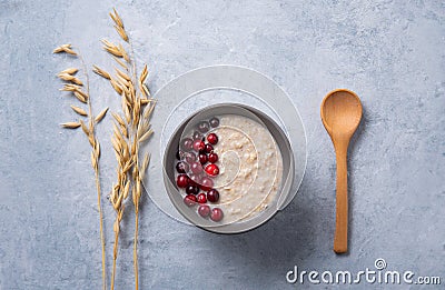 Healthy oats porridge with cranberries on light blue background with oatmeal ears and wood spoon. Healthy breakfast diet food Stock Photo