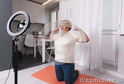 a healthy pensioner sits on the bedroom floor in front of a tripod for a camera, shoots a fitness video tutorial for the Stock Photo