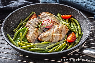 Healthy recipe of grilled chicken, green vegetable and tomatoes on a dark nonstick pan placed on metalic grid and dark Stock Photo