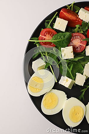 healthy salad of arugula spinach tomatoes feta cheese and boiled eggs in a black round kitchen plate, top view. useful on a diet Stock Photo