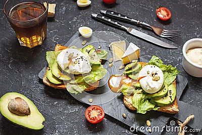 Healthy sandwich - poached eggs and avocado on toast with tomatoes on black stone background Stock Photo