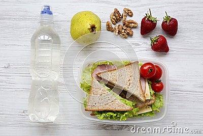 Healthy school lunch box with fresh organic vegetables sandwiches, walnuts, bottle of water and fruits on white wooden background, Stock Photo