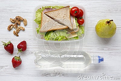 Healthy school lunch box with fresh organic vegetables sandwiches, walnuts, bottle of water and fruits on white wooden background, Stock Photo