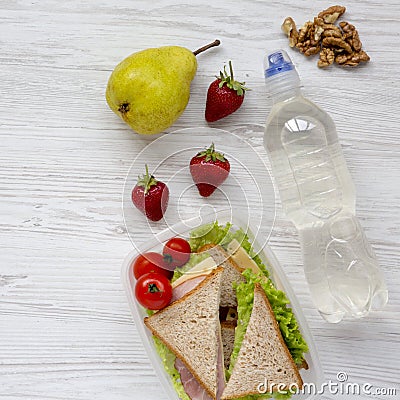 Healthy school lunch box with fresh organic vegetables sandwiches, walnuts, bottle of water and fruits on white wooden table, over Stock Photo