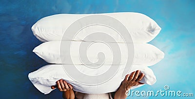 Healthy sleep, woman holds pile of folded white pillows in her hands on blue background Stock Photo