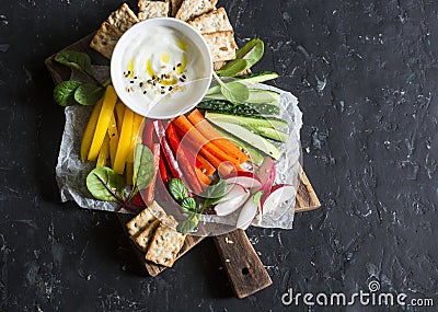 Healthy snack - raw vegetables and yogurt sauce on a wooden cutting board, on a dark background, top view. Vegetarian healthy food Stock Photo