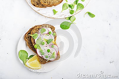 Healthy snack: slice grain bread with ricotta, green peas, radishes, lemon zest and juice. Top view Stock Photo