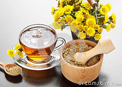 Healthy tea, bucket with coltsfoot flowers and mortar on table Stock Photo