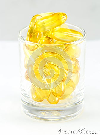 Healthy vitamin glass : yellow oil pills in translucent glass Stock Photo