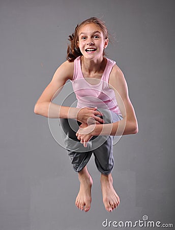 Healthy young happy smiling teenage girl skipping and dancing in studio. Child exercising with jumping on grey background. Stock Photo