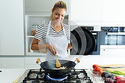 Healthy young woman cooking and mixing food in frying pan in the kitchen at home. Stock Photo