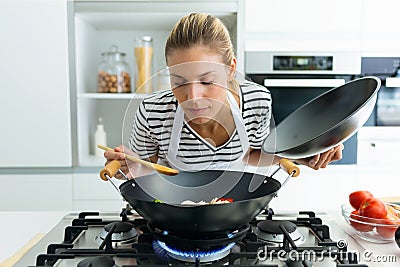 Healthy young woman cooking and smelling food in frying pan in the kitchen at home. Stock Photo