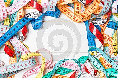 Heap of colorful measuring tapes in the form of frame on wooden background. Top view of slim waist concept with copy space Stock Photo