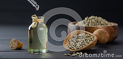 Heap of dried organic hemp seeds or cannabis plant seeds in spoon and bowl with glass of hemp seed oil on wooden backdrop Stock Photo