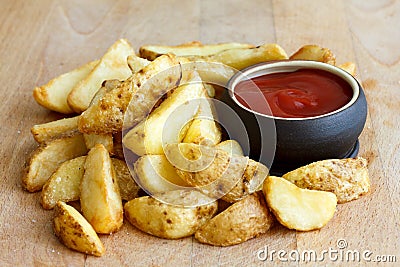 Heap of fried potato wedges on wood board with ketchup dip in bo Stock Photo