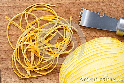 Heap of peeled lemon zest on wood chopping board next to half of peeled lemon and zester from above Stock Photo