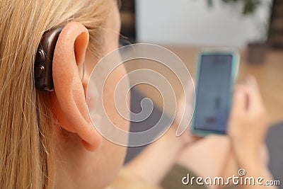 Hearing impaired woman working with smartphone. Close up of blonde woman wearing hearing aid on ear and pressing button while Stock Photo