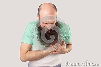 Heart attack or infarct. Portrait of sick middle aged bald bearded man in green t-shirt standing and holding his chest because Stock Photo