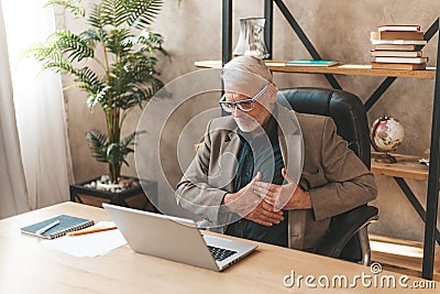 Heart attack at work in the office. Senior man holding his sternum with his hands, pain and discomfort Stock Photo