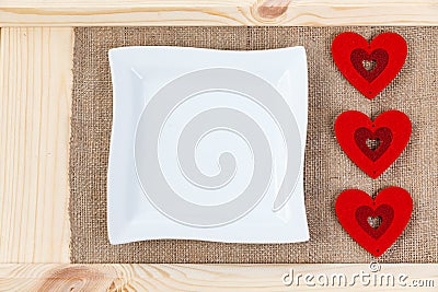 Heart on a background of wood covered with burlap, white square plate a card for Valentine`s Day. Stock Photo